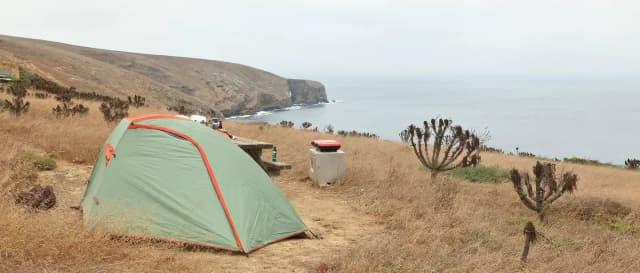 Tent sitting in dried grass on a ocean bluff overlooking the coastline