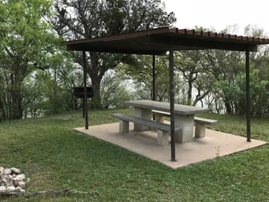 RV site with covered picnic table, grill, and Waco Lake in the background
