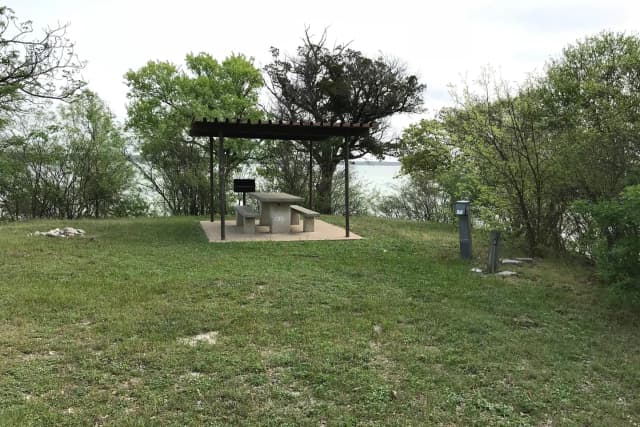 RV site with covered picnic table, grill, and Waco Lake in the background
