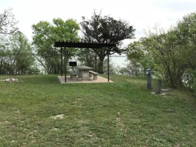 RV site with covered picnic table, grill, and Waco Lake in the background