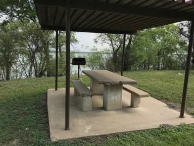 RV site with covered picnic table, grill, and Waco Lake in the background