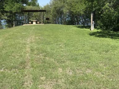 RV site with covered picnic table, grill, and Waco Lake in the background
