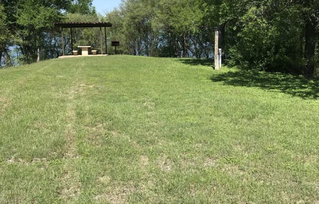 RV site with covered picnic table, grill, and Waco Lake in the background