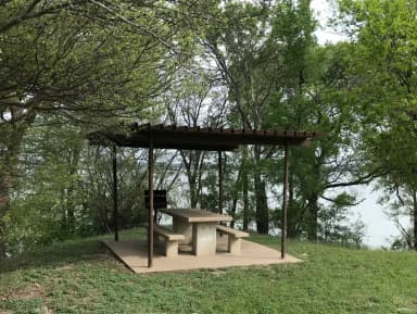 RV site with covered picnic table, grill, and Waco Lake in the background