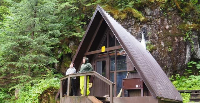Two people by railing of entrance to Mount Flemer Cabin with trees in background