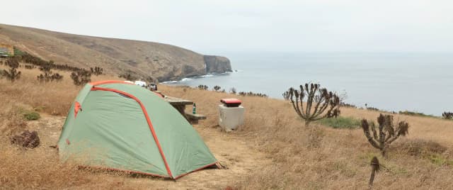 Tent sitting in dried grass on a ocean bluff overlooking the coastline