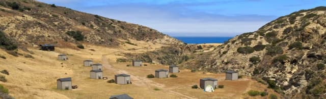 Eight foot tall wind shelters on a dry, grassy terrace overlooking the ocean.