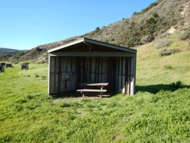 Eight foot tall wind shelter with picnic table surrounded by green grass.