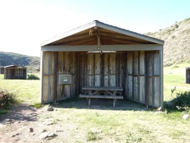 Eight foot tall wind shelter with picnic table surrounded by green grass.