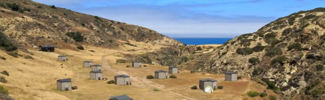 Eight foot tall wind shelters on a dry, grassy terrace overlooking the ocean