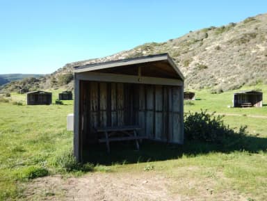 Eight foot tall wind shelter with picnic table surrounded by green grass.