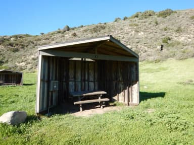 Eight foot tall wind shelter with picnic table surrounded by green grass.