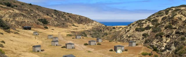 Eight foot tall wind shelters on a dry, grassy terrace overlooking the ocean