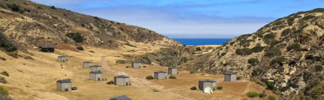 Eight foot tall wind shelters on a dry, grassy terrace overlooking the ocean