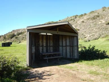 Eight foot tall wind shelter with picnic table surrounded by green grass.