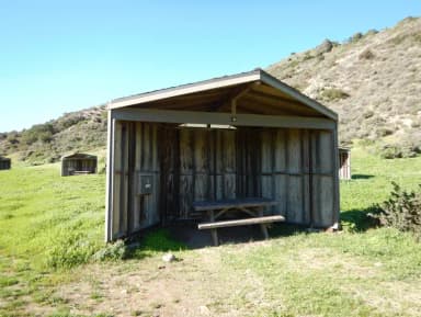 Eight foot tall wind shelter with picnic table surrounded by green grass.