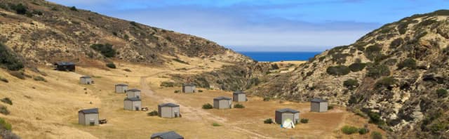 Eight foot tall wind shelters on a dry, grassy terrace overlooking the ocean