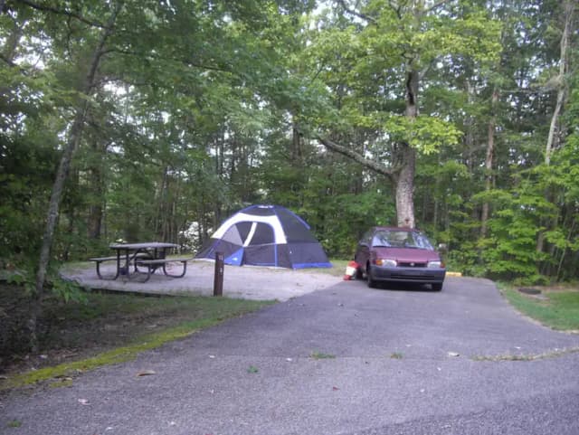 Little car parked on next to family size tent on tent pad on a gravel pad.
