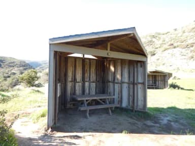 Eight foot tall wind shelter with picnic table surrounded by green grass.