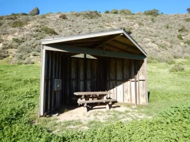 Eight foot tall wind shelter with picnic table surrounded by green grass.