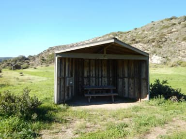 Eight foot tall wind shelter with picnic table surrounded by green grass.
