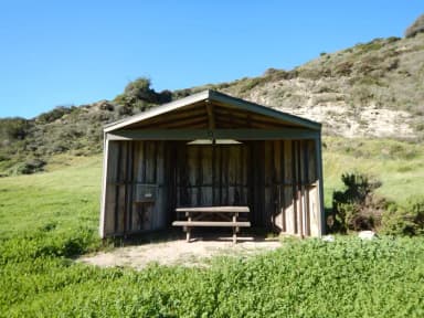 Eight foot tall wind shelter with picnic table surrounded by green grass.