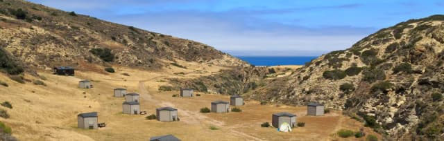 Eight foot tall wind shelters on a dry, grassy terrace overlooking the ocean.