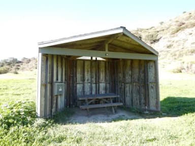 Eight foot tall wind shelter with picnic table surrounded by green grass.