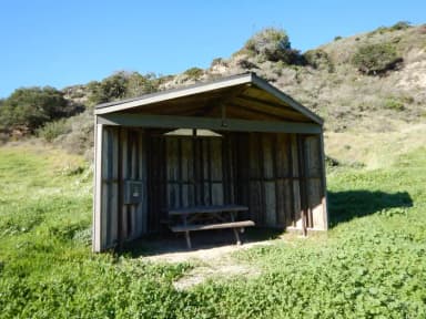 Eight foot tall wind shelter with picnic table surrounded by green grass.