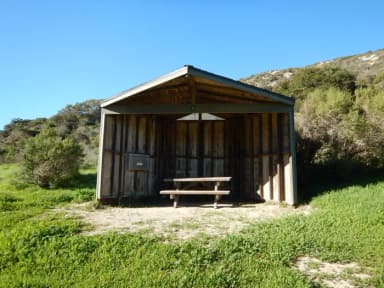 Eight foot tall wind shelter with picnic table surrounded by green grass.