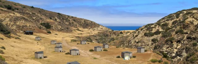 Eight foot tall wind shelters on a dry, grassy terrace overlooking the ocean.