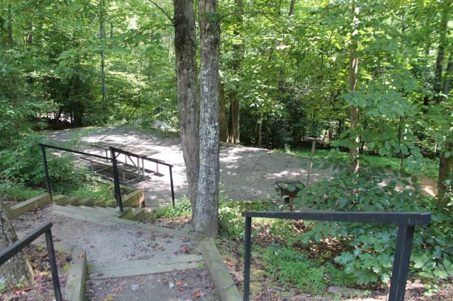 Gravel site with table, grill, fire pit with steps leading down from parking