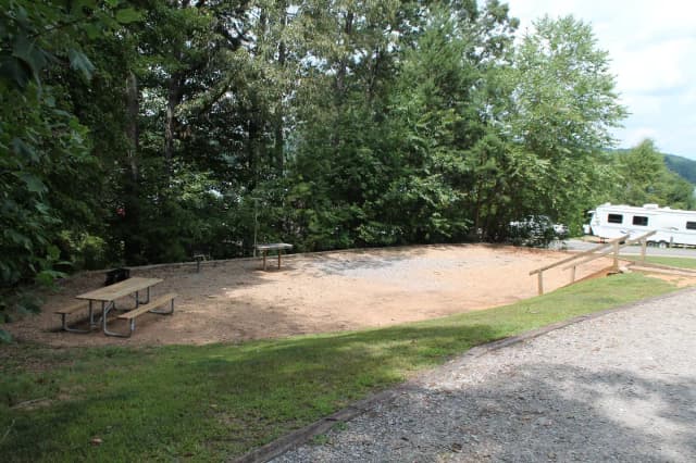 Gravel site with steps going down to table, grill, and fire pit surrounded by trees