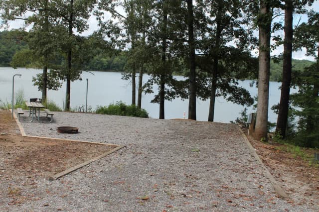 Short gravel pull in to site with table, fire pit, and grill with views of the lake