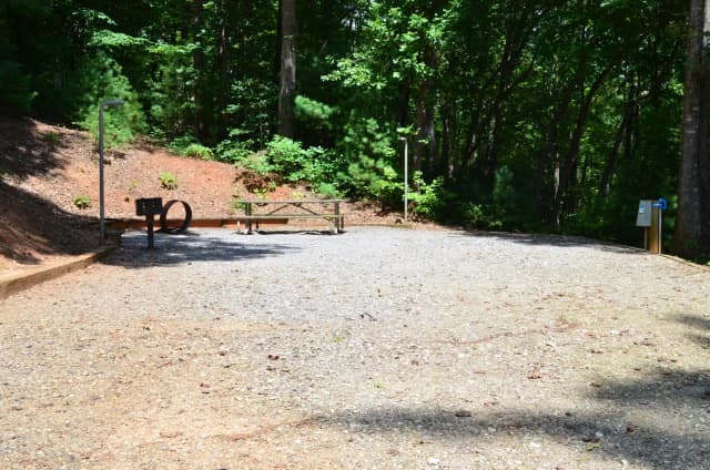 Gravel site with fire pit, table, grill, surrounded by trees