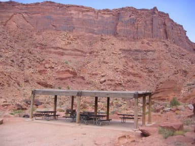 Close up of the Big Bend Group Site C shade shelter and picnic tables. Large, red rock cliff walls in the distance.