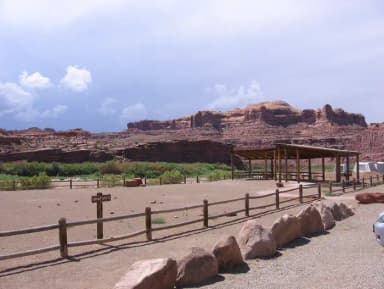 Gold Bar Group Site C large shade shelter and picnic tables with the Colorado River flowing nearby and tall, red rock cliffs in the distance.