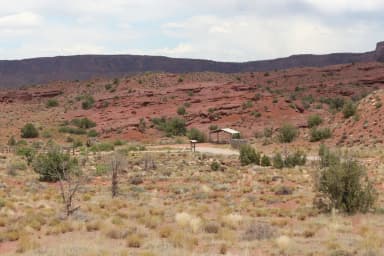 The Upper Onion Group Site A is tucked into the side of a hill. Vegetation in the area includes small shrubs covering most of the ground, with the occasional juniper tree dotting the landscape.