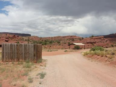 Large shade shelter with picnic tables underneath and a toilet nearby at the Upper Onion Creek Group Site B. In the distance, shrub-covered hills with juniper trees dotting the landscape.