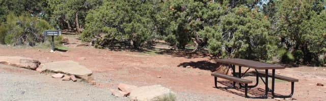Loop B Site 39 with a brown metal picnic table and a grill, set against red dirt and surrounded by juniper trees.