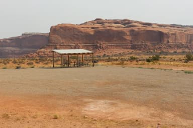 Lone Mesa Group Site B shade shelter and picnic tables. Red rock cliffs in the distance.