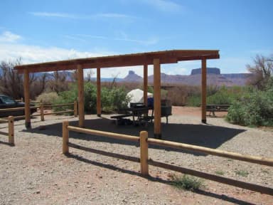Close up of the Lower Onion Creek Group Site A shade shelter, picnic and picnic tables with views of Castleton Tower in the distance.