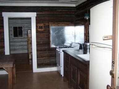 A galley kitchen inside a historic cabin with a refrigerator, sink, countertop, and stove for guests.