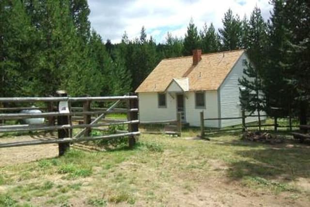White cabin in meadow with rail fence and pine trees