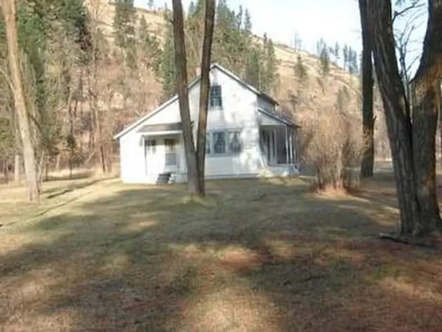 White cabin on flat ground in an open forest of conifers and deciduous trees and shrubs with no leaves.