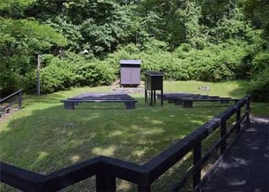 Campground amphitheater. Wooden boardwalk leading to open grass area with 10 wooden benches facing wooden projection screen.  Dense green vegetation is behind theater.
