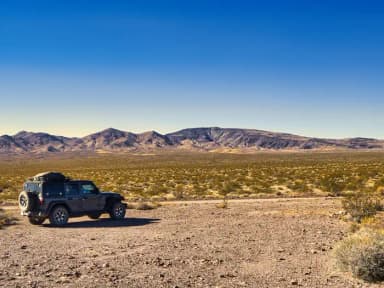 4-wheel drive vehicle parked along the side of Greenwater Valley Road with Black Mountains in the background., filed by the agency against 9 campsites at Death Valley Backcountry Roadside Camping